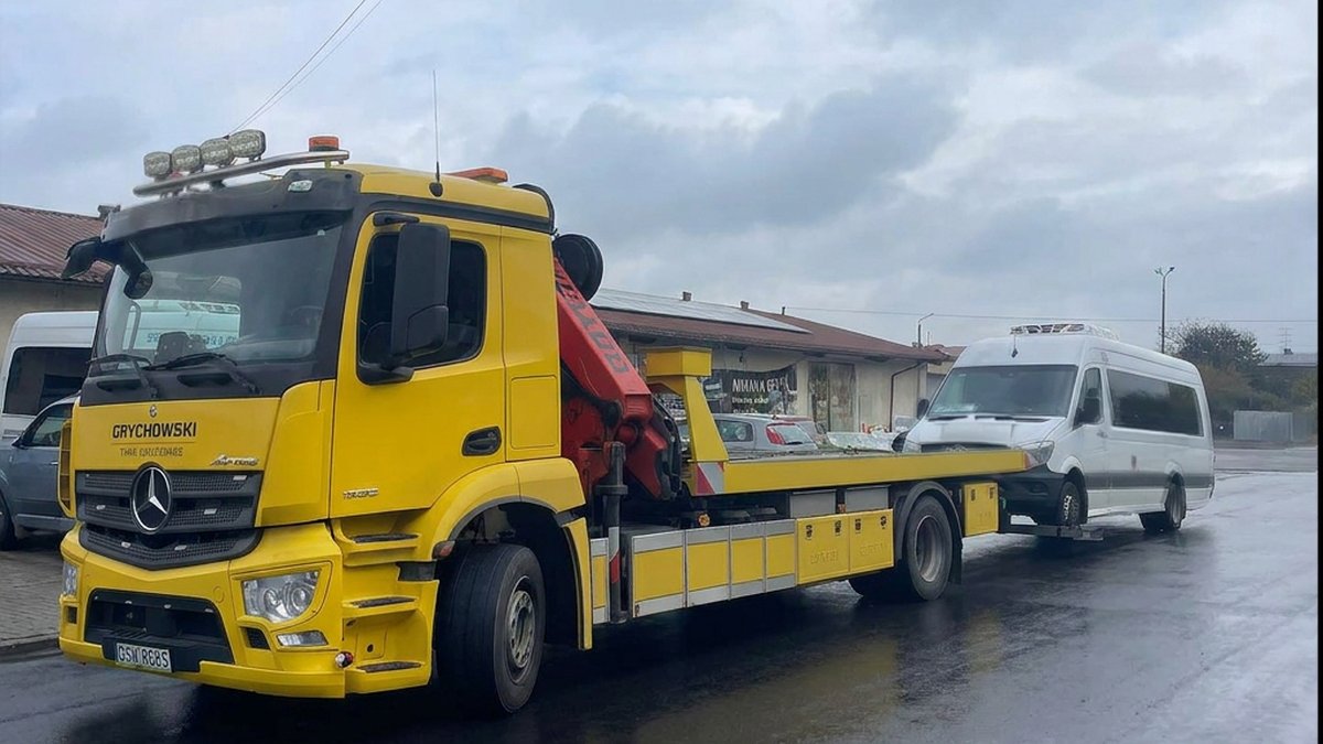 Laweta Grychowski Pomoc Drogowa Rawicz holująca busa dostawczego po awarii — mokra droga, pochmurne niebo